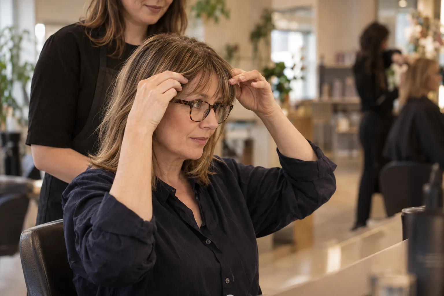 Woman in her fifties checking how her maxi fringe sits above her glasses in a Bristol salon mirror